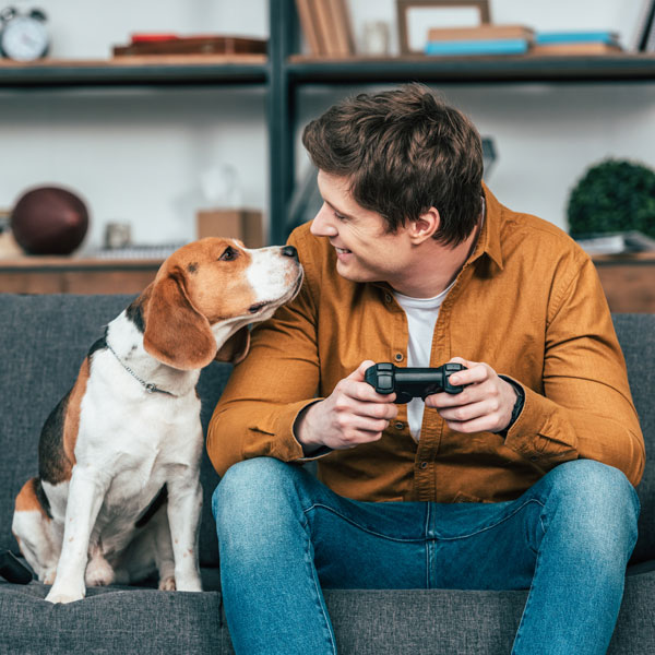 A man and his dog playing video games on a couch.