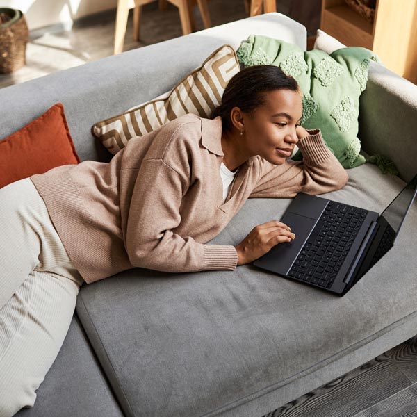 Woman lounging on couch with laptop, applying for retail credit.